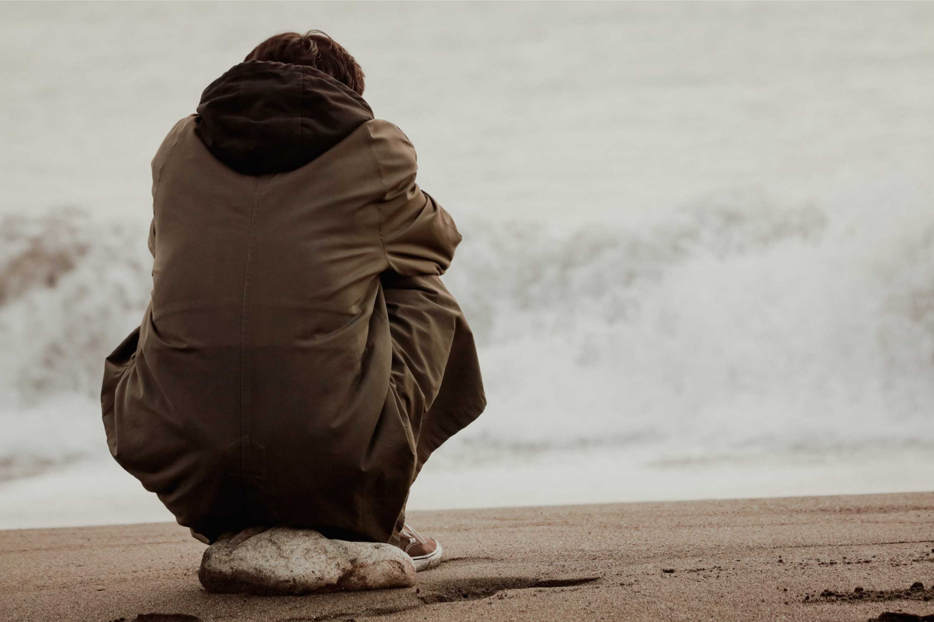 Mann sitzt auf einem Stein und schaut auf das Meer hinaus mit seinem Kopf auf seinem Schoß gestützt