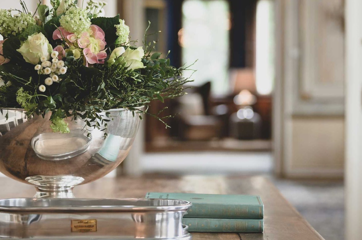 Im Ambiente eines Wohnzimmers stehen frische Blumen in einer Vase neben Büchern zum lesen auf dem Tisch.
