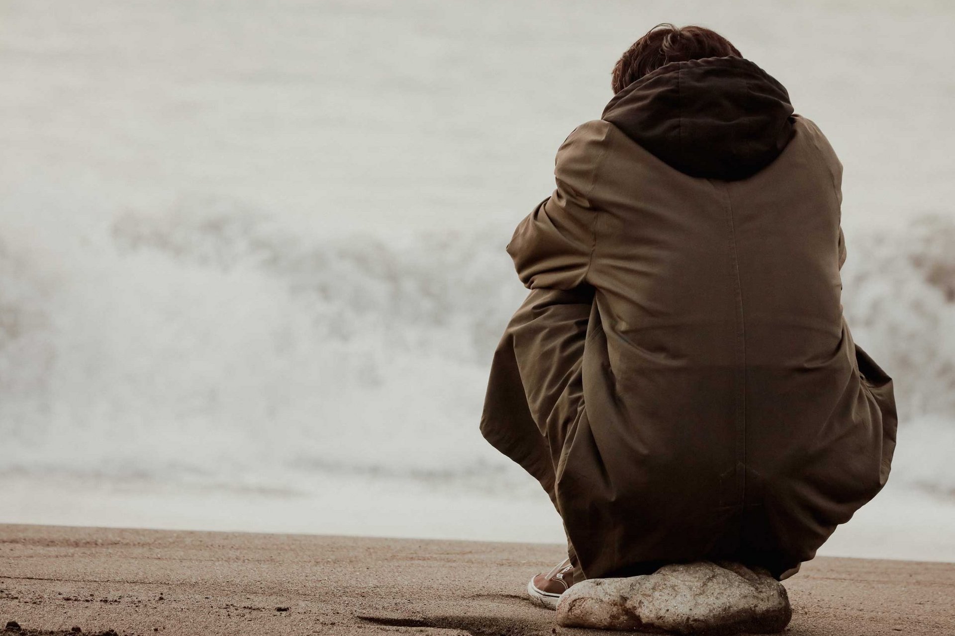 Ein Mann sitzt allein, ohne soziale Kontakte am Umfeld und starrt regungslos auf das Meer hinaus.