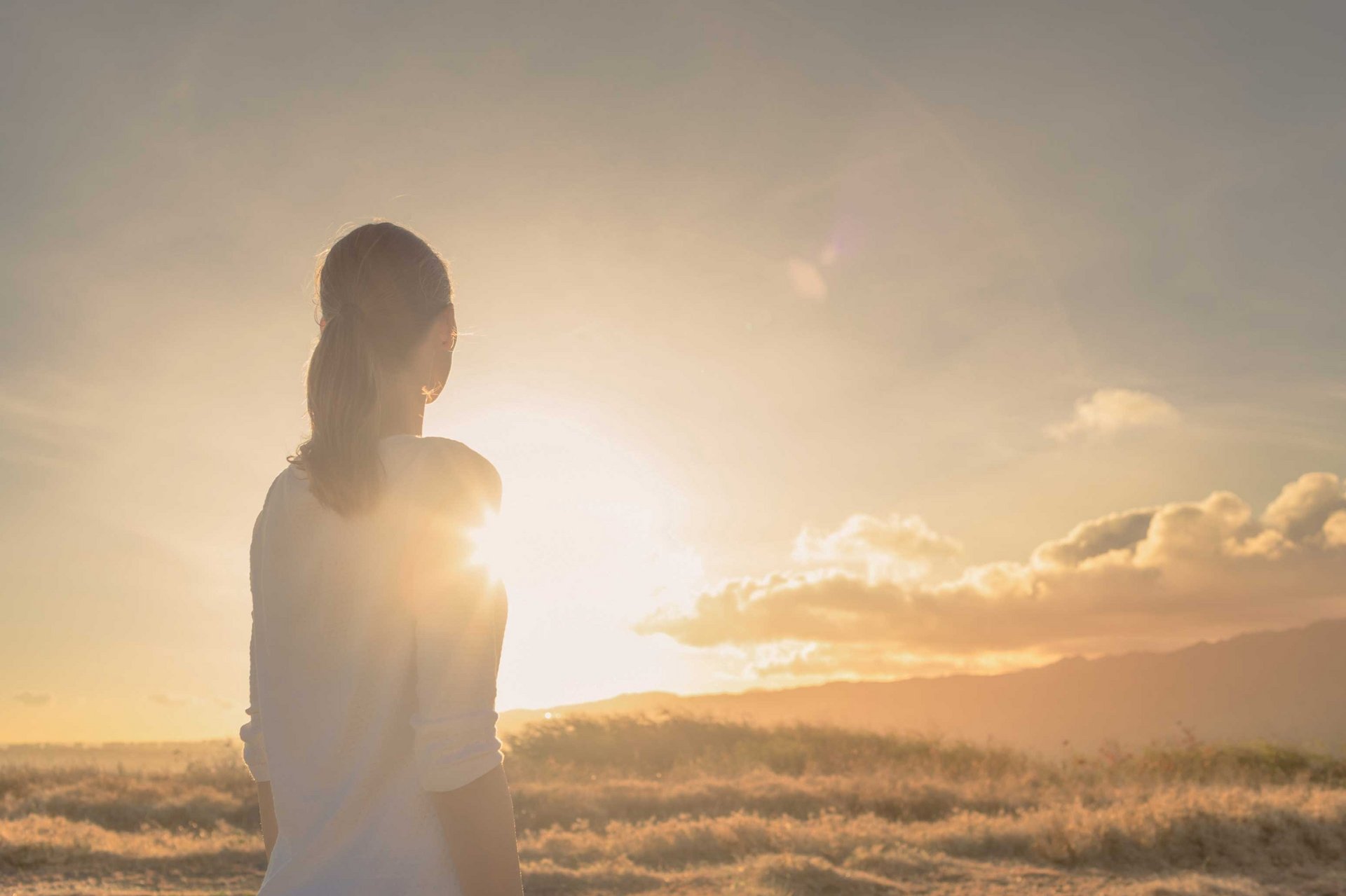 Eine Frau steht auf einem Feld und schaut in den Sonnenuntergang.