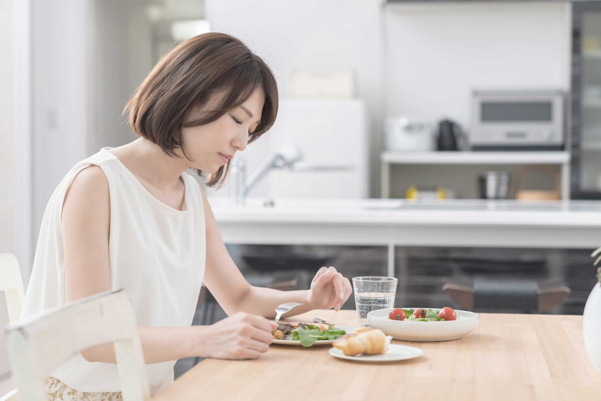 Frau sitzt vor vollen Tellern, kann aber nicht essen