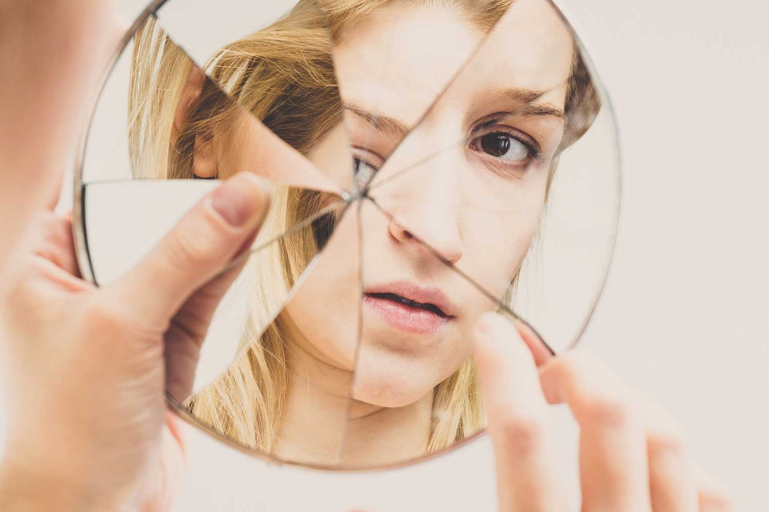 Frau schaut in einen zerbrochenen runden Spiegel als Versinnbildlichung, dass der Körper der Spiegel der Seele ist