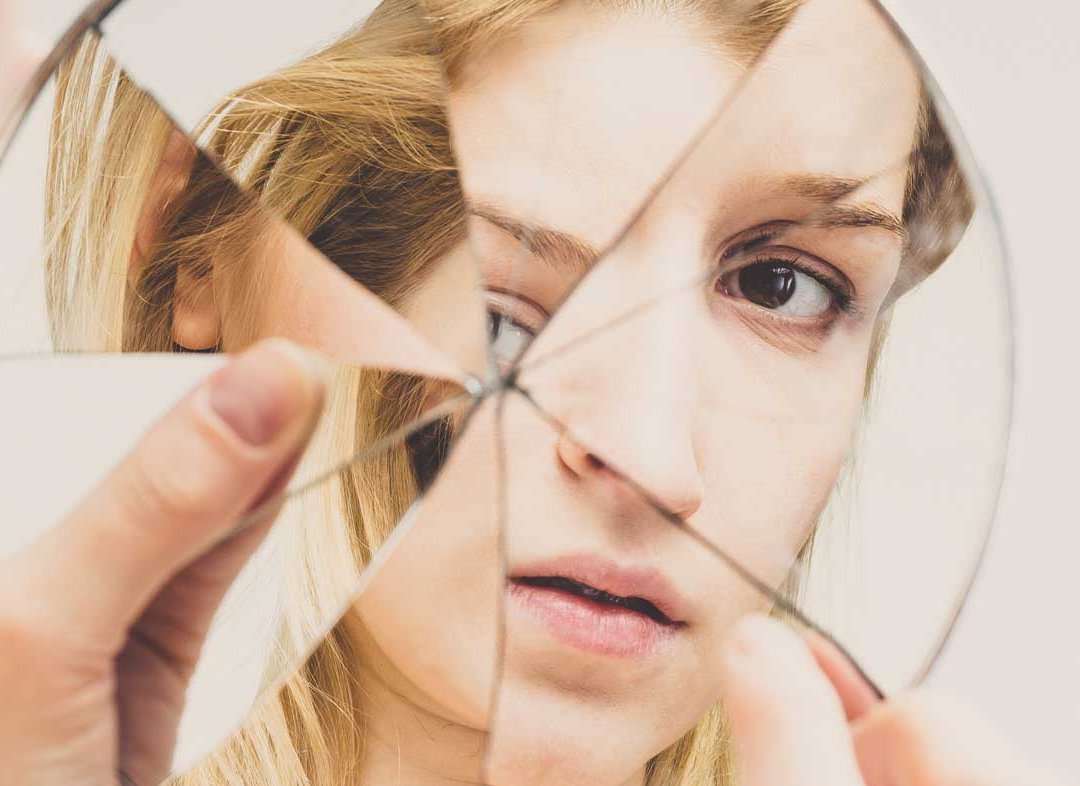 Eine Frau erblickt sich selbst in einem zerbrochenen Spiegel