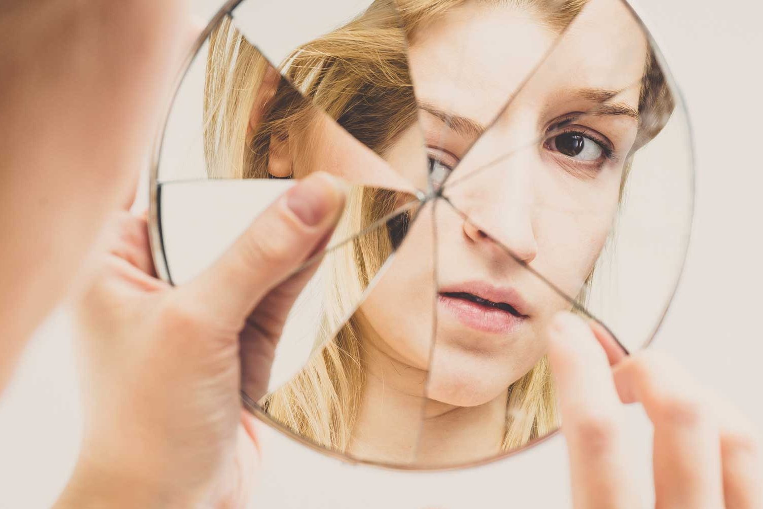 Eine Frau erblickt sich selbst in einem zerbrochenen Spiegel