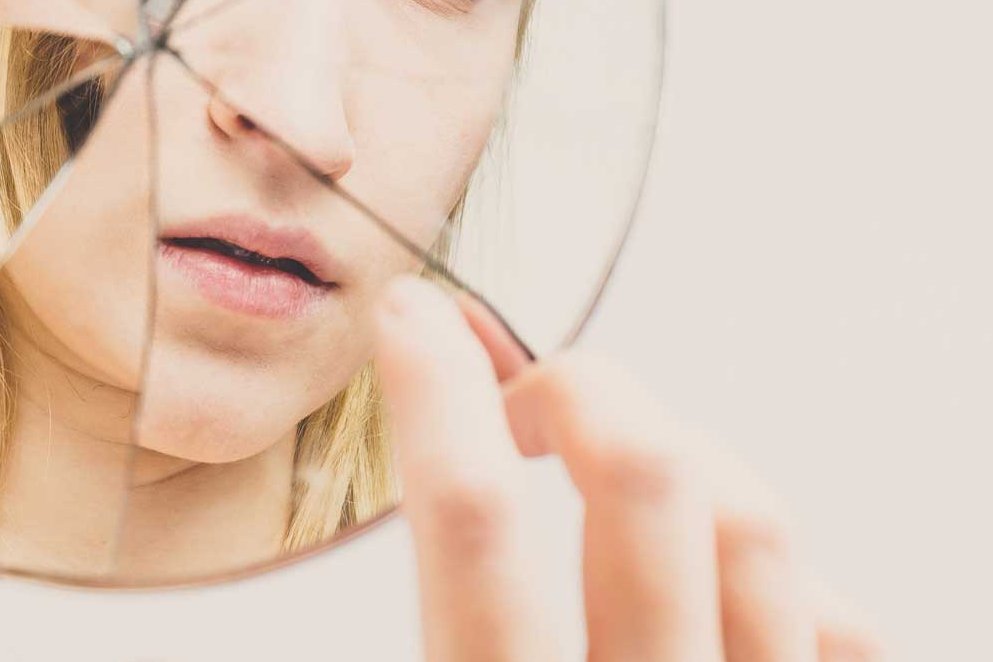 Eine Frau erblickt sich selbst in einem zerbrochenen Spiegel und berührt diesen mit dem Finger