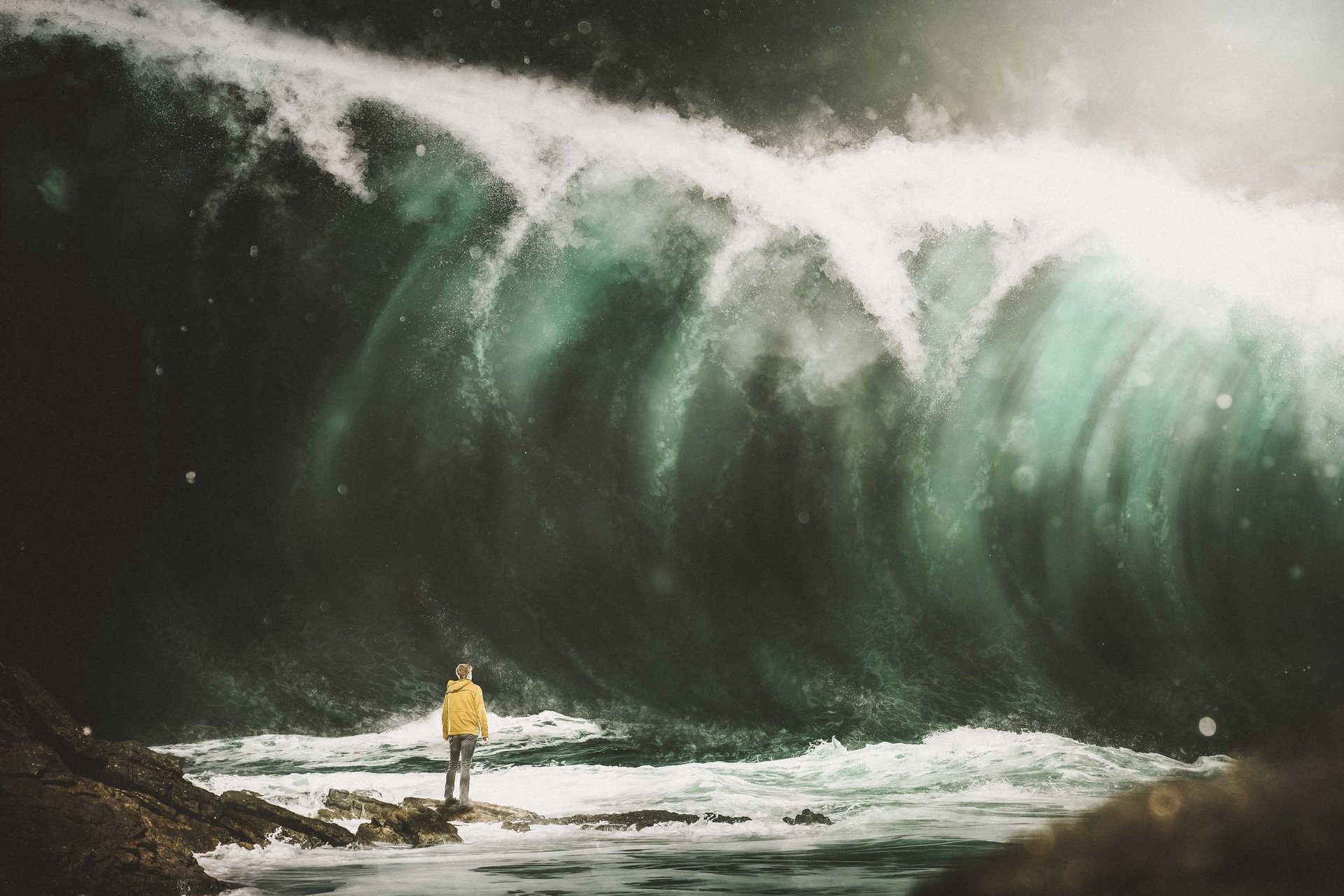 Mann steht am Strand vor einer großen Welle