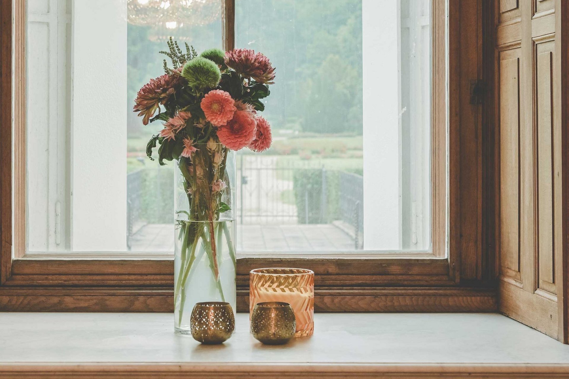 Frische, farbenfrohe Blumen stehen auf einer Fensterbank, daneben Kerzen.