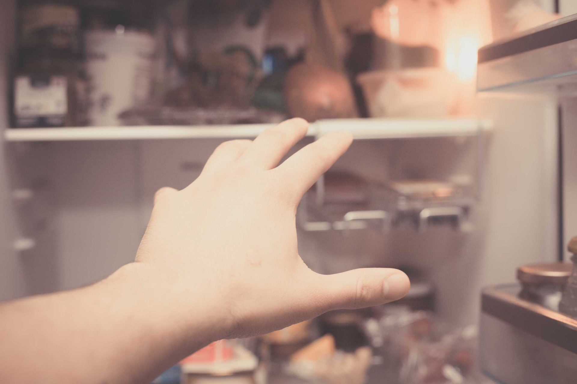 Eine Hand greift voll Verlangen in den offenen Kühlschrank