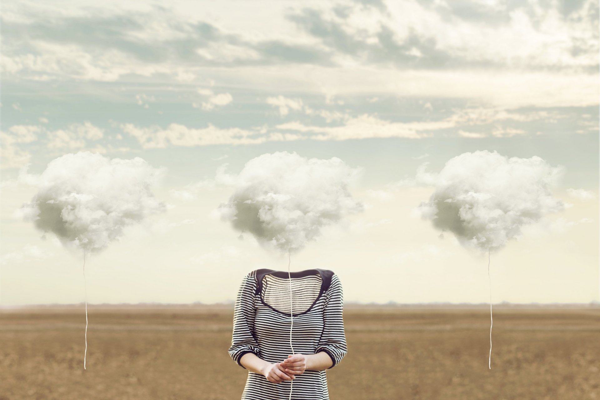 Eine Person steht auf einem Feld und hält eine Wolke am Faden in der Hand, welche den Kopf ersetzt.