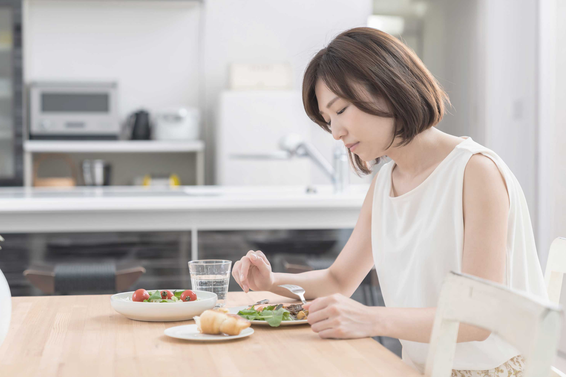 Eine Frau sitzt vor Tellern mit Essen und schaut zweifelnd.
