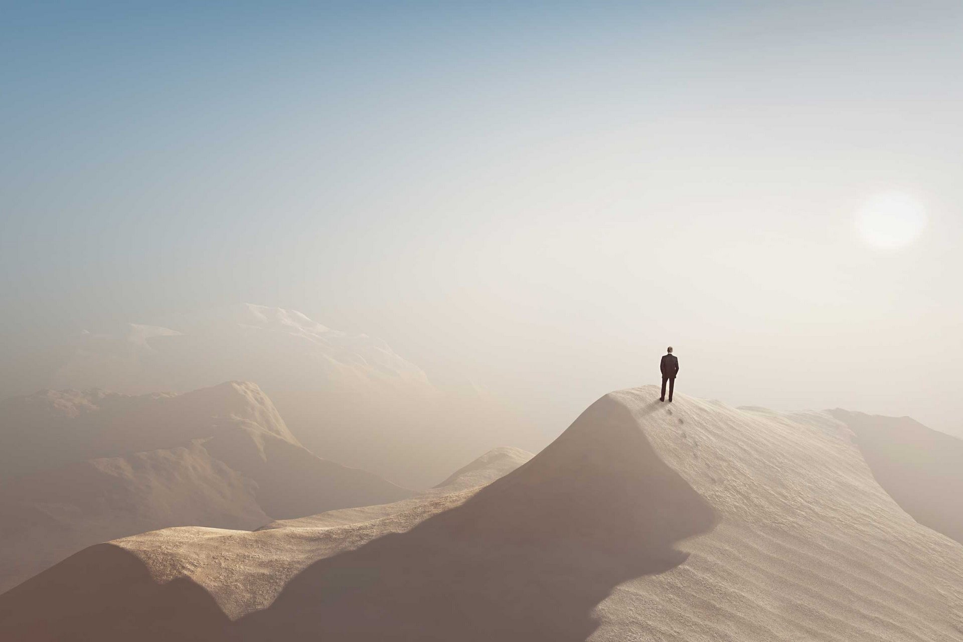 Ein Mann im Anzug steht einsam auf einem Berg inmitten einer Wüste