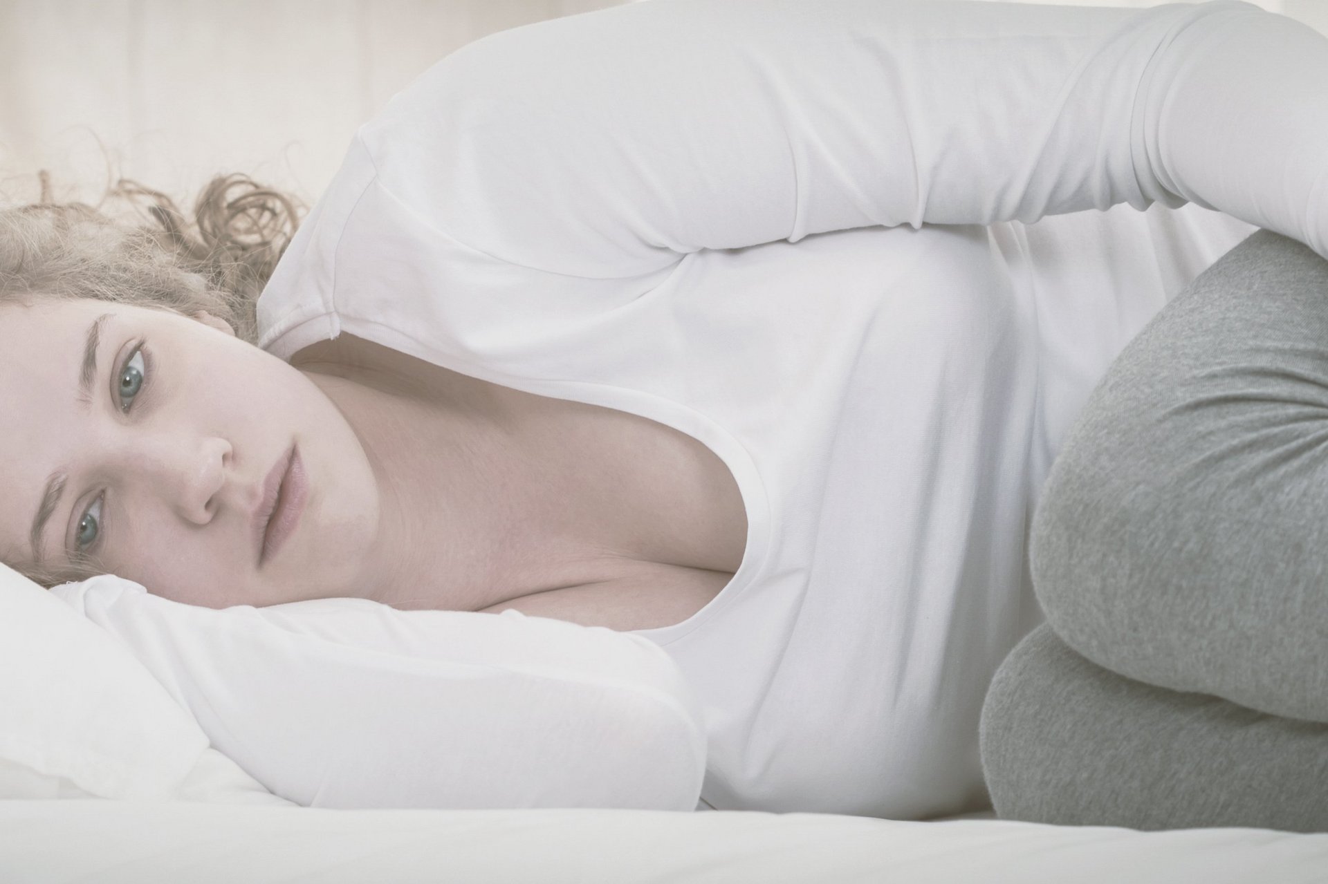 Eine Frau liegt in Embryonalstellung im Bett und starrt ins Leere