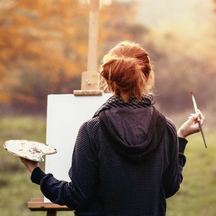 Eine Frau malt an einer Staffelei im Freien.