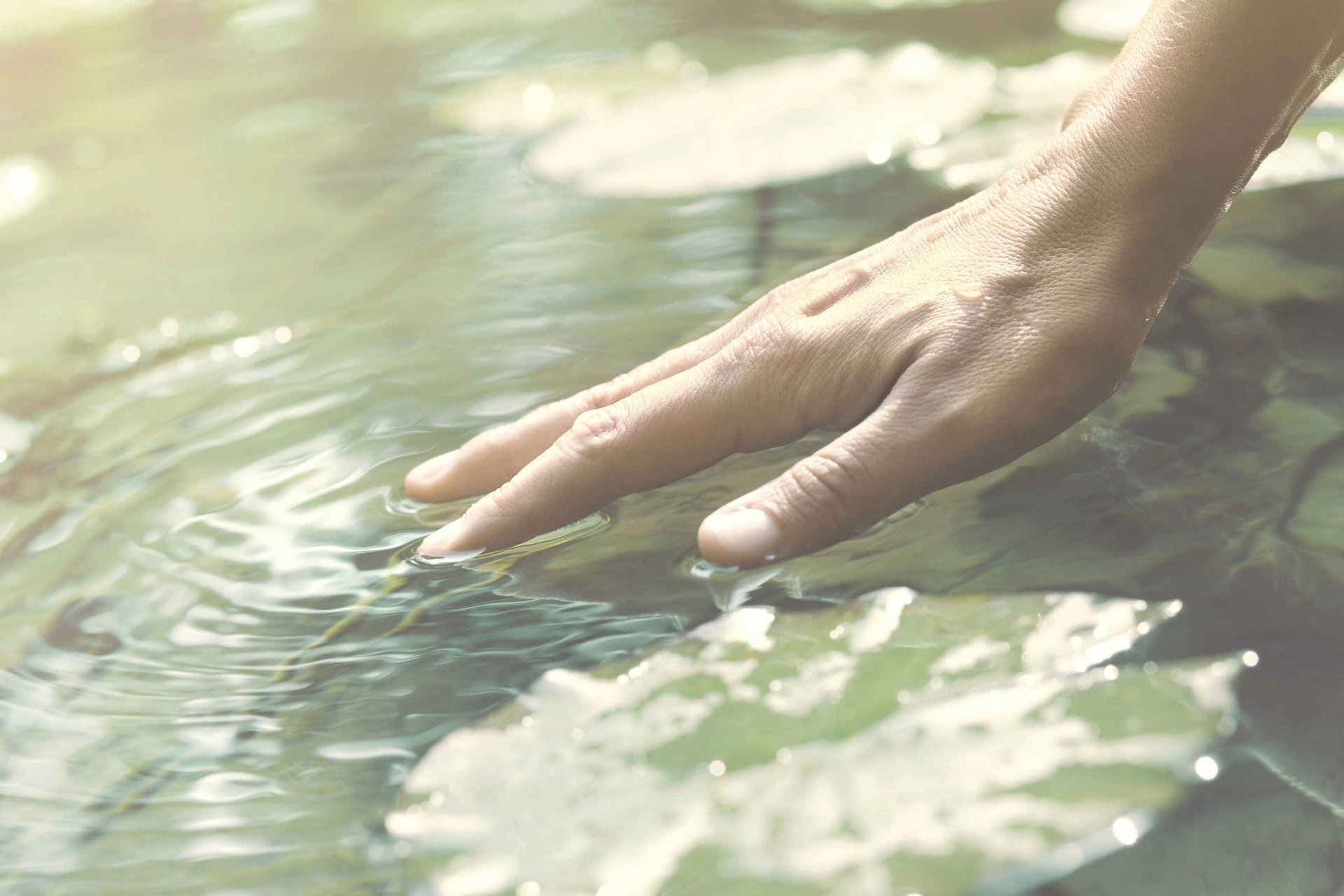 Eine Hand berührt oberflächlich das Wasser.