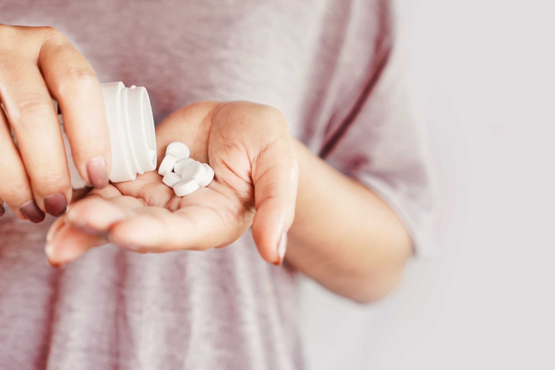 Frau verteilt Tabletten aus einer Dose auf Ihrer Hand