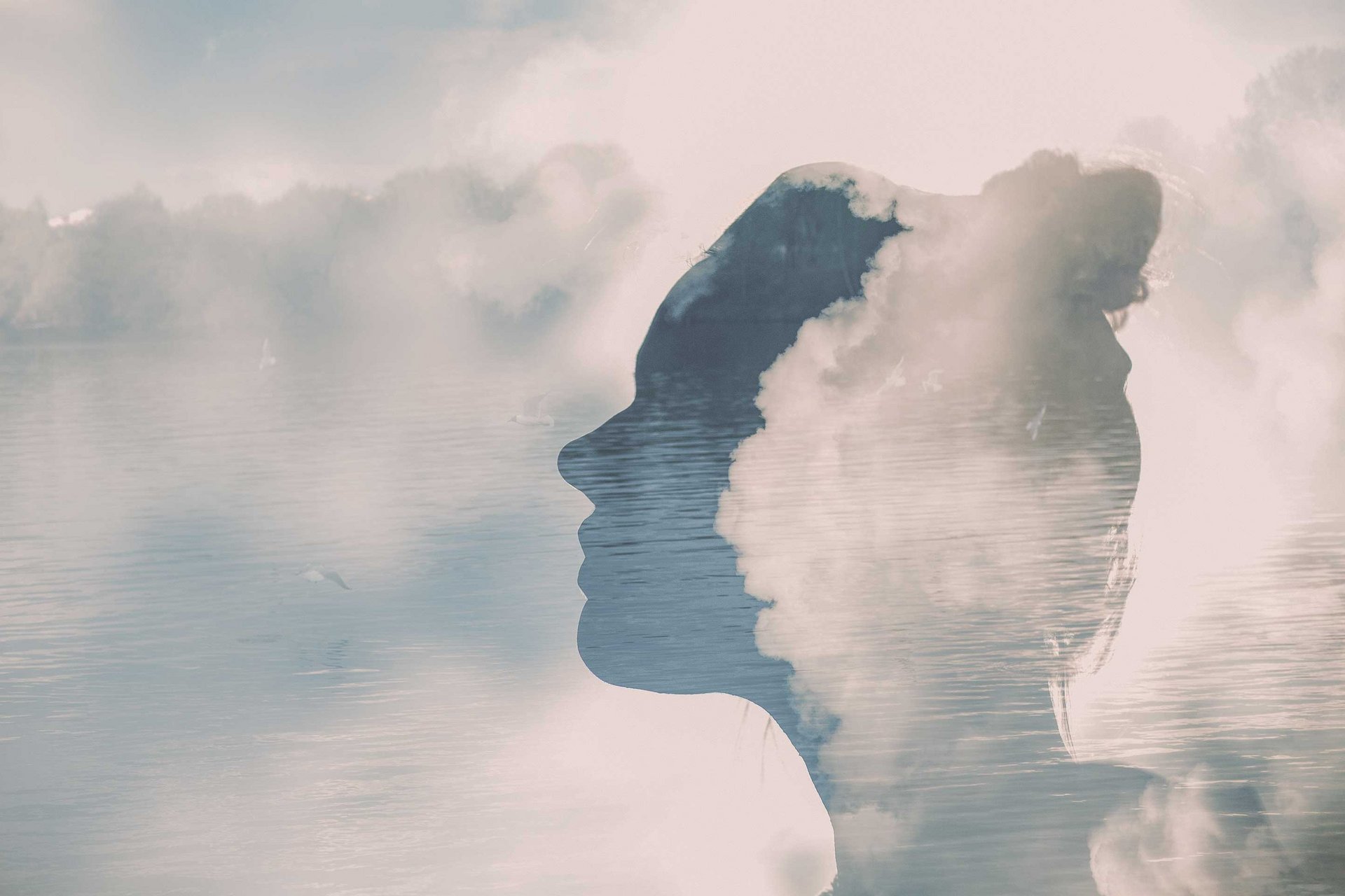 Silhouette einer Frau vor einem Wasser von dem Nebel aufsteigt