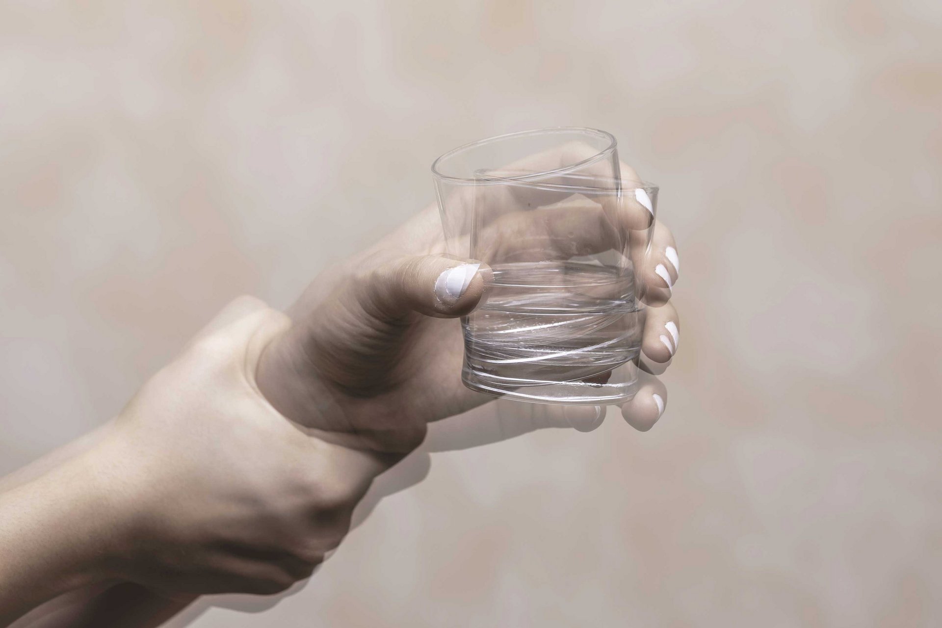 Eine Person hält ein Wasserglas in der zittrigen Hand.