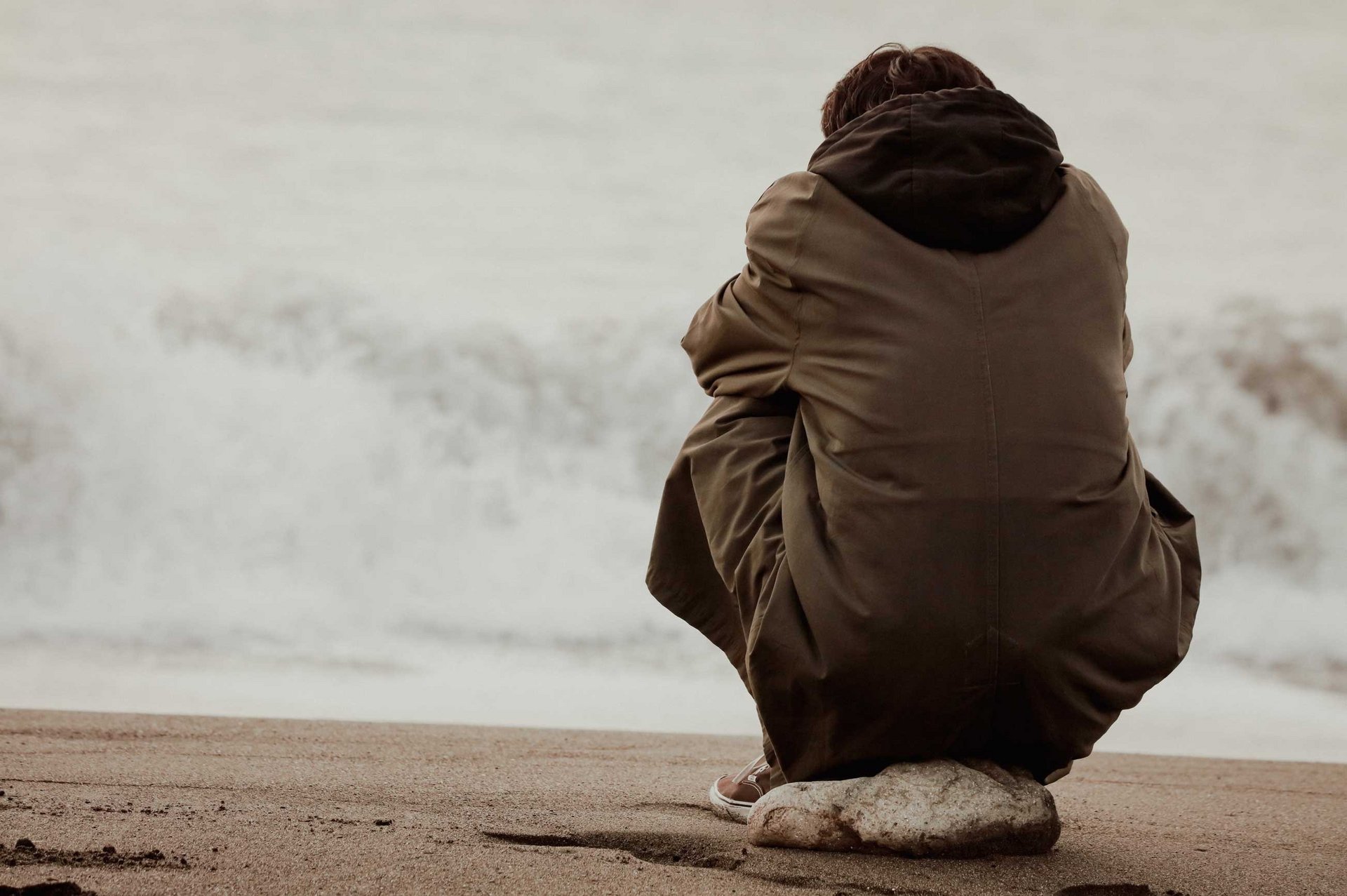 Ein Mann sitzt allein, ohne soziale Kontakte am Umfeld und starrt regungslos auf das Meer hinaus.