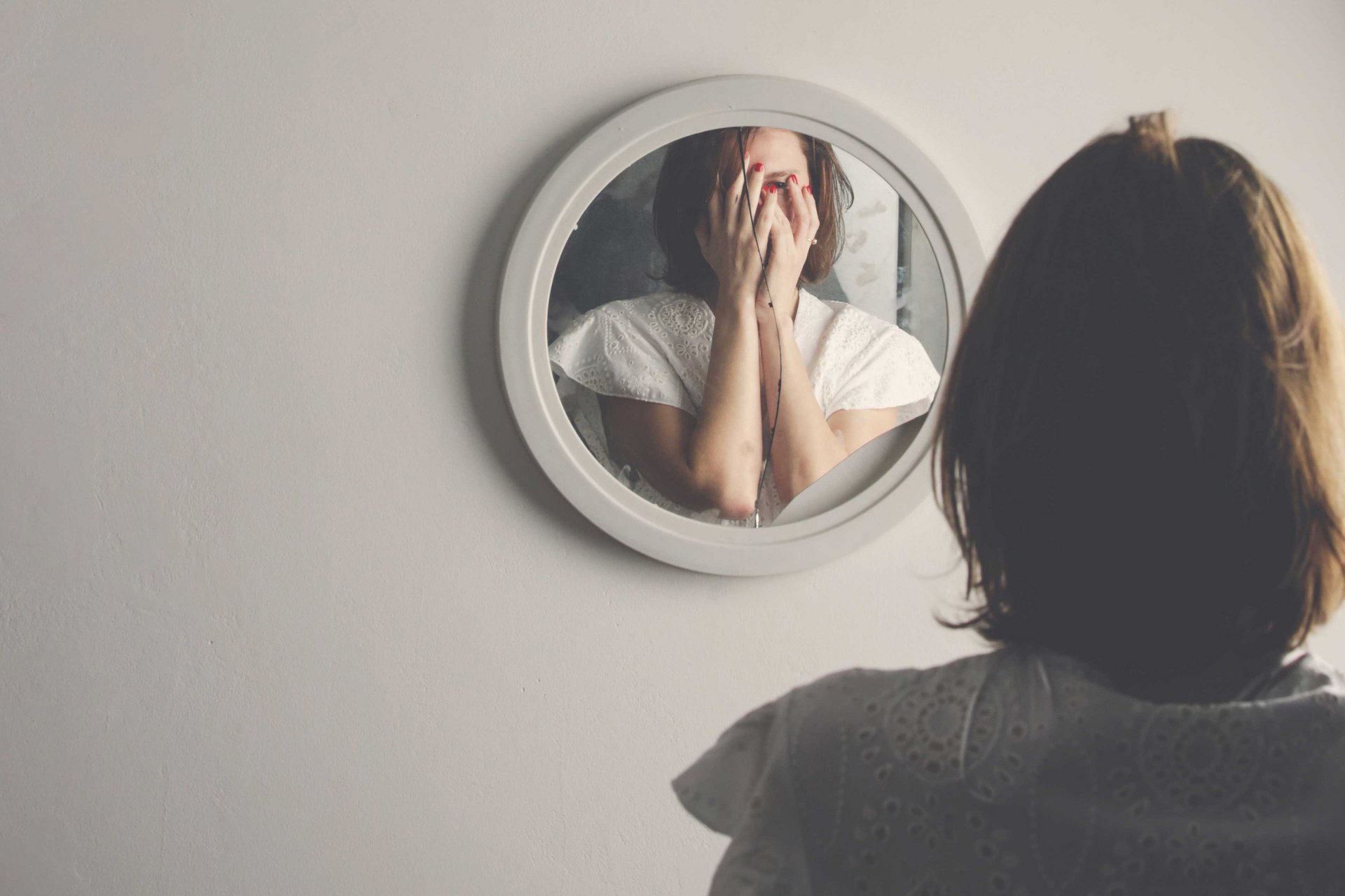 Eine Frau hält sich die Hände vor das Gesicht und steht vor einem zerbrochenen Spiegel.