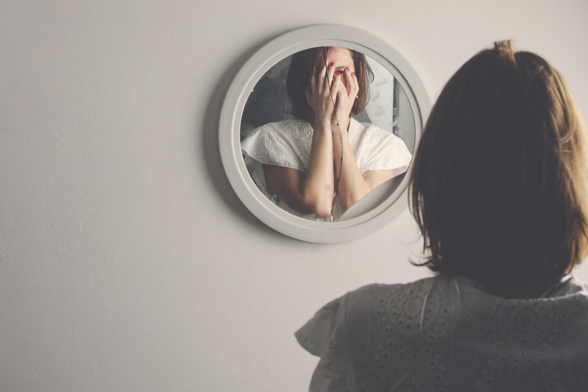 Eine Frau steht verzweifelt vor einem zerbrochenen Spiegel.