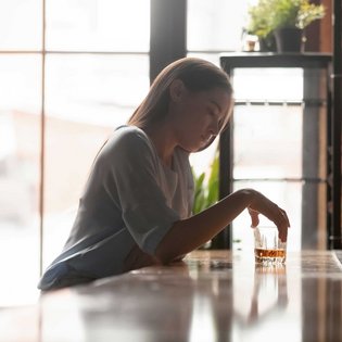 Eine Frau sitzt an einem Tresen und grübelt über das Glas Whiskey vor sich nach.