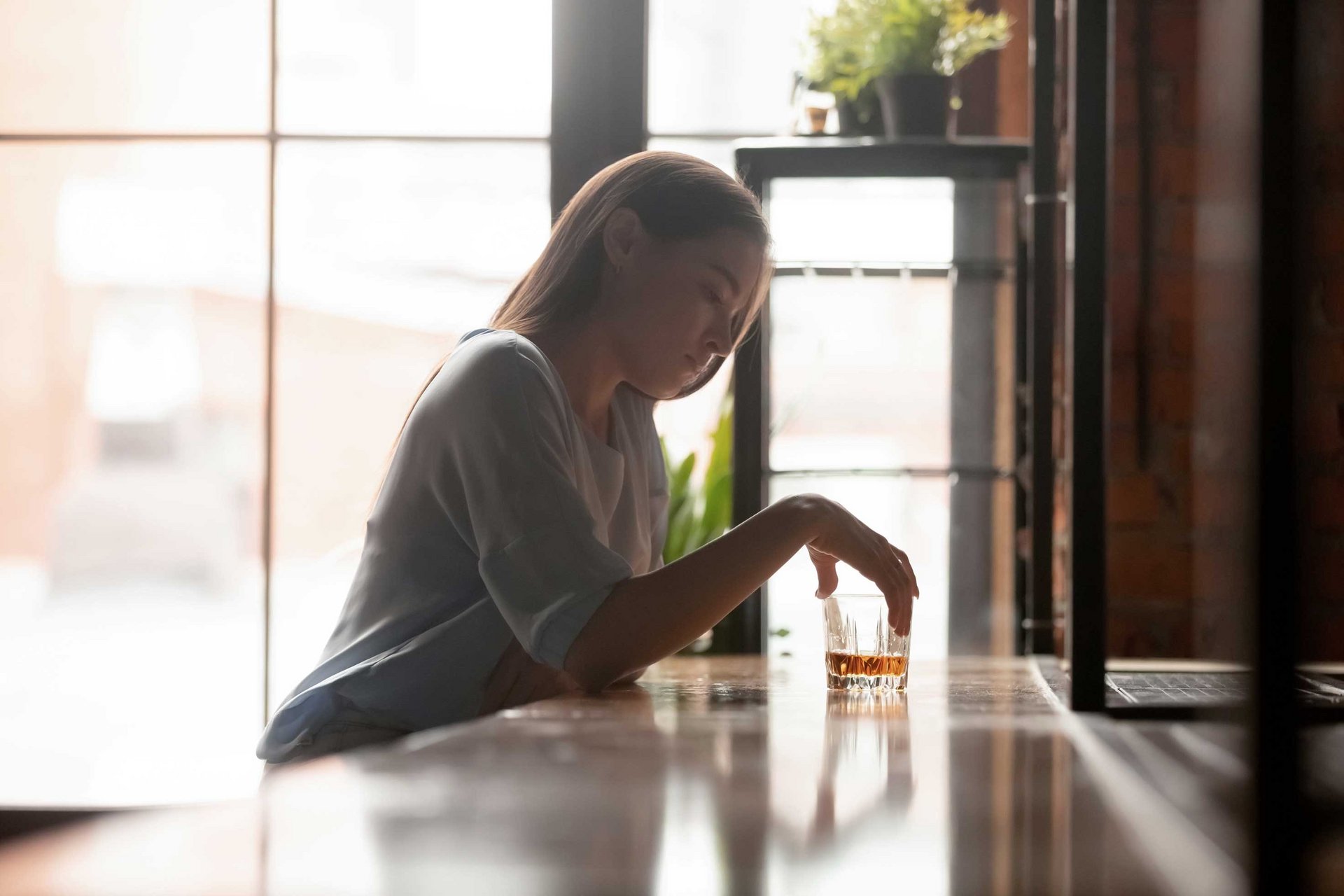 Frau sitzt in einer Bar und wirkt gedankenverloren beim Konsumieren eines alkoholischen Getränks als Versinnbildlichung von Alkohol als Auslöser der Appetitlosigkeit