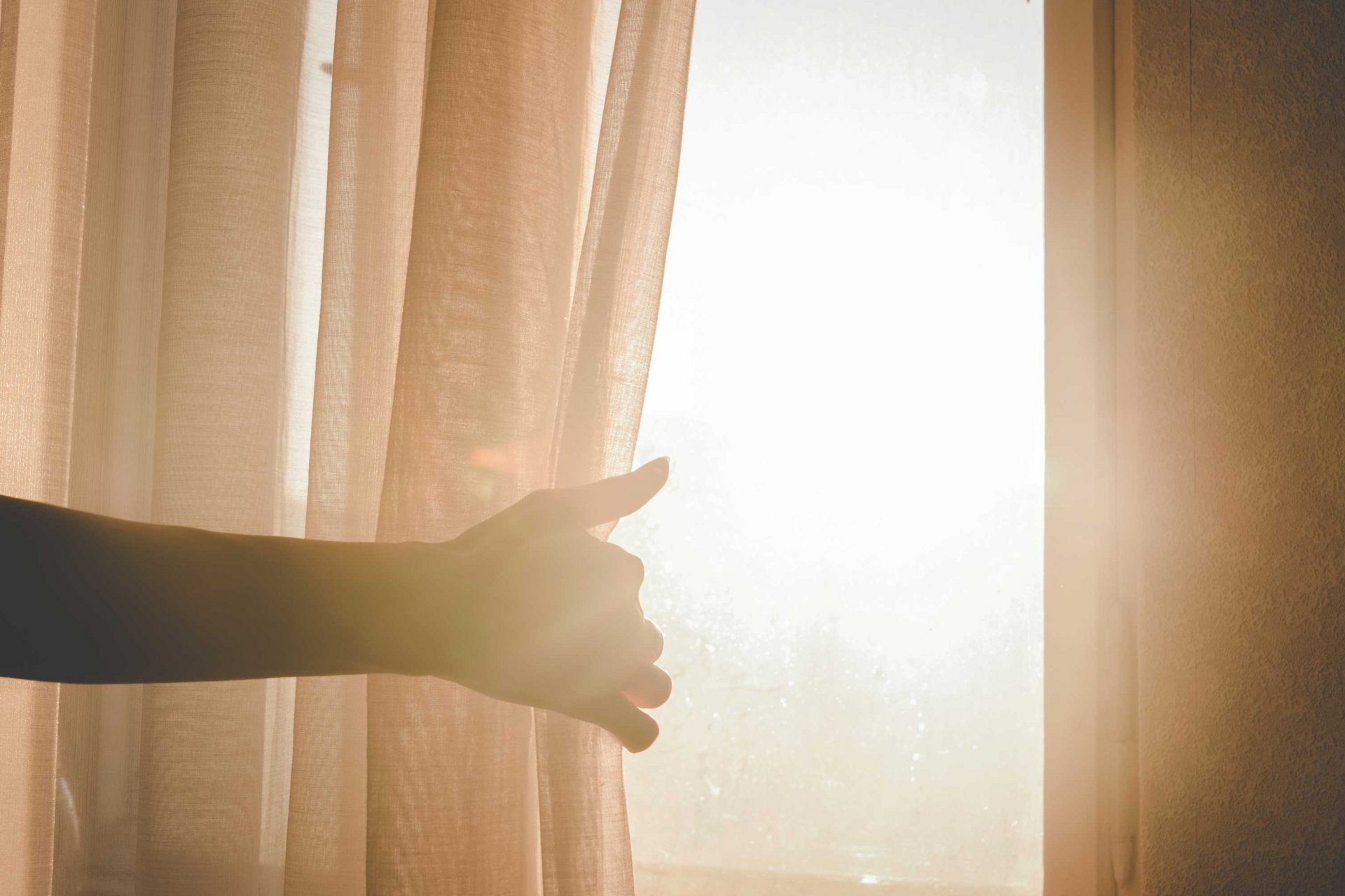 Eine Person macht einen Vorhang auf, sodass Sonnenlicht in den Raum strahlt.