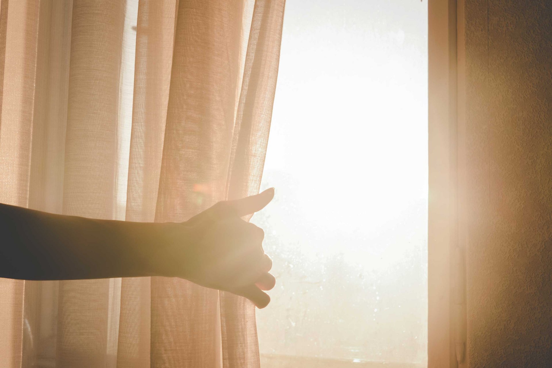 Eine Hand zieht einen Vorhang auf, damit Sonnenlicht in den Raum kommt.