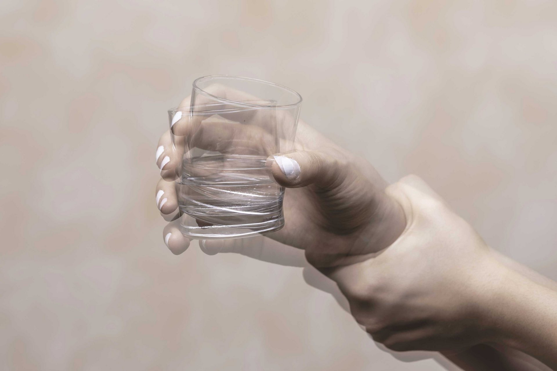 Eine Hand mit einem Wasserglas zittert, sie wird von einer anderen Hand festgehalten und beruhigt