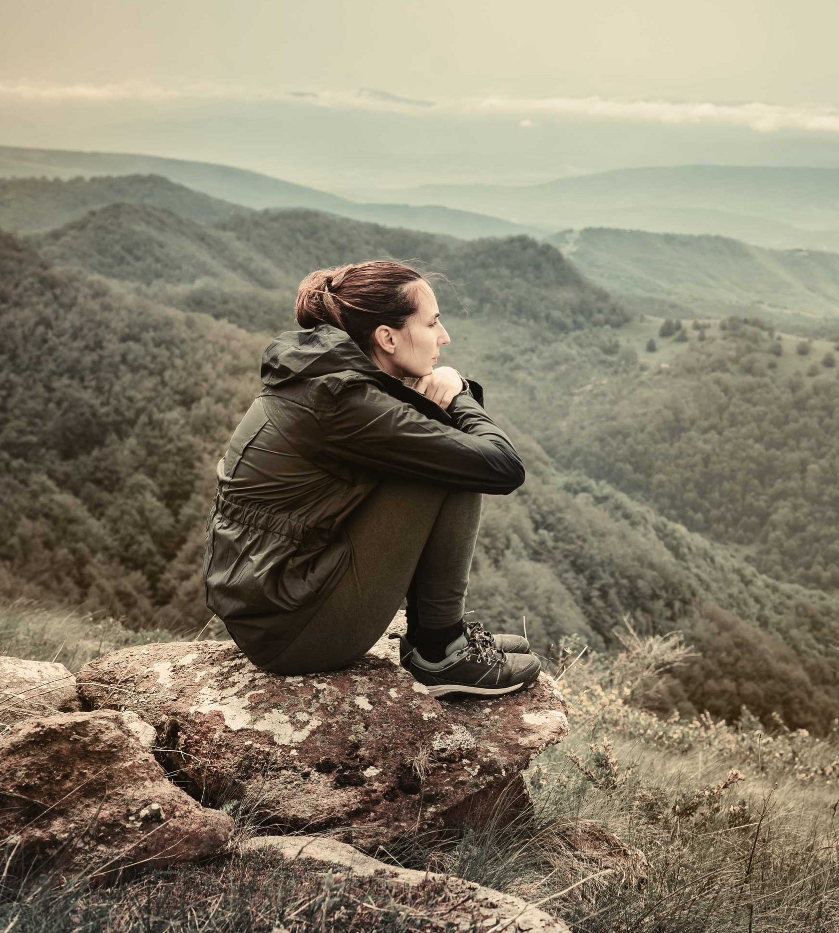 Frau sitzend auf einem Berg mit den Armen um Ihre Beine geschlungen versinnbildlicht seelische Symptome