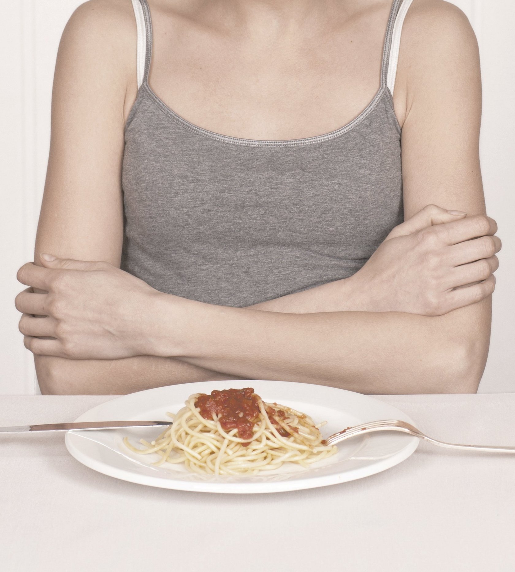 Frau mit verschränkten vor einem Teller Spaghetti Bolognese versinnbildlicht die Appetitlosigkeit